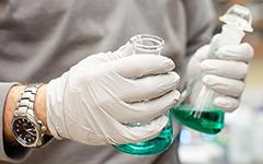 Gloved hands holding beakers in lab.