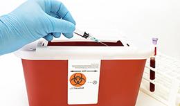 Hand putting needle in biohazard box